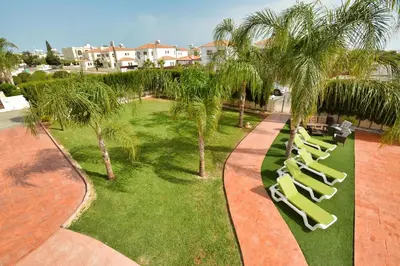 a row of lounge chairs on a lawn with palm trees at Villa Eva in Ayia Napa