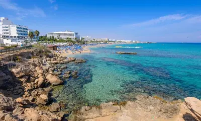 a beach with blue water and rocks and buildings at Sunset Villa Protaras in Protaras