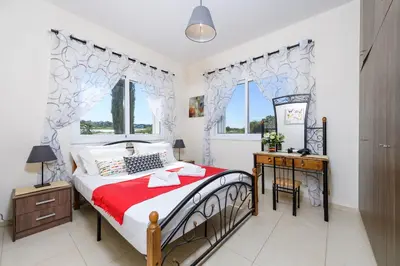 a bedroom with a bed and a desk and two windows at Sunset Villa Protaras in Protaras