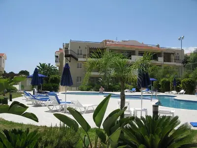 a swimming pool with chairs and umbrellas and a building at Pyla Gardens A101 in Pyla
