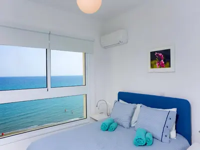 a bedroom with a blue bed and a large window at On The Beach Penthouse by TrulyCyprus in Limassol