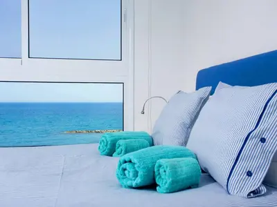 a bed with blue and white pillows and the ocean at On The Beach Penthouse by TrulyCyprus in Limassol