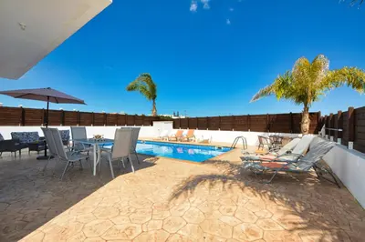 a patio with a table and chairs next to a pool at Nissi Villa Gintare in Ayia Napa