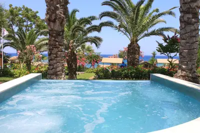 a pool with palm trees and the ocean in the background at Crystal Springs Beach Hotel in Protaras