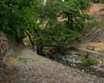 a wooden bridge over a stream with a bench at Theoxenia in Kalopanayiotis