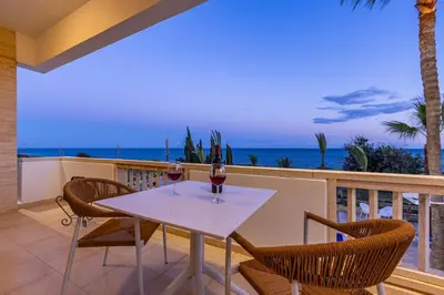 a table with two wine glasses on a balcony with the ocean at Villa Chrysta in Ayios Theodhoros