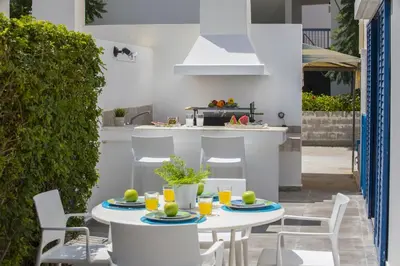 a patio with white tables and chairs and a kitchen at Protaras Villa Loulla in Protaras