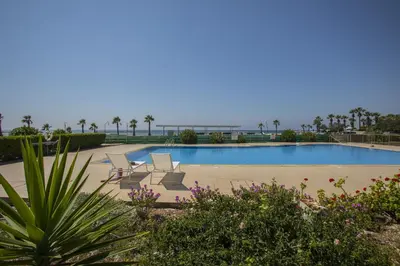 a pool with lounge chairs and the ocean in the background at Larnaca Sunshore Beachfront Suite in Voroklini
