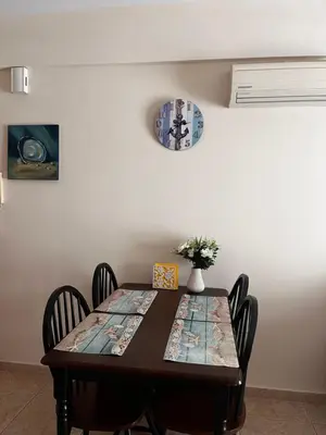 a dining room table with chairs and a clock on the wall at Makenzy Apartment in Larnaka