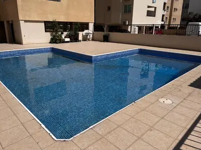 a large swimming pool with blue tiles on the ground at Makenzy Apartment in Larnaka