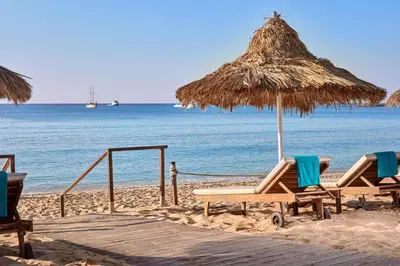 a beach with chairs and a straw umbrella and the ocean at Ha.De.Co. Holiday Apts in Ayia Napa