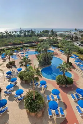 an aerial view of a resort pool with blue chairs and palm trees at Nissiana Hotel & Bungalows in Ayia Napa