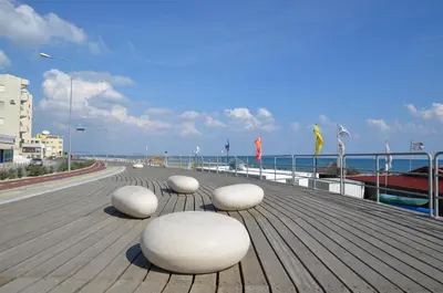 four white chairs sitting on a boardwalk near the ocean at Mackenzie Blu Beach Studio in Larnaka