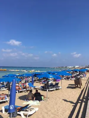 a group of people sitting on a beach with blue umbrellas at Amigos Apartment Mythical in Protaras