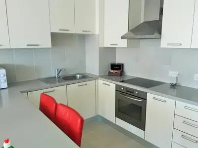 a kitchen with white cabinets and a sink and a red chair at 16 SANDY BEACH in Larnaka