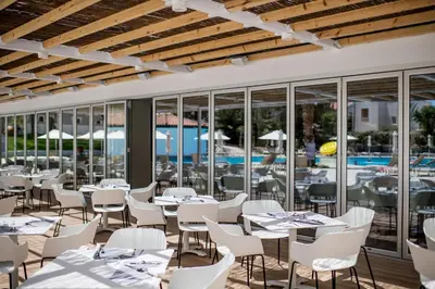 a restaurant with white tables and chairs and a pool at Narcissos Waterpark Resort in Protaras