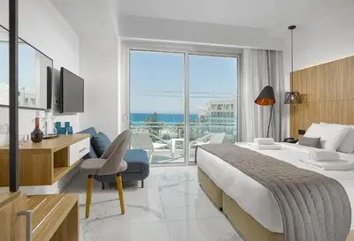 a hotel room with a bed and a desk and a television at The Blue Ivy Hotel & Suites in Protaras