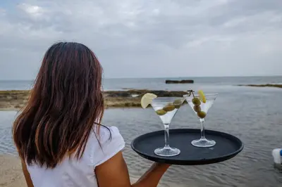 a woman holding a tray with two martini glasses on the beach at Thalassines Villas in Ayia Napa