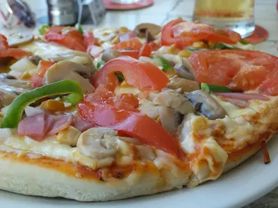 a pizza with tomatoes and mushrooms on a plate at Livas Hotel Apartments in Protaras