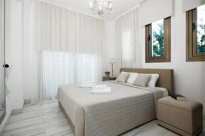 a white bedroom with a large bed and a chair at Villa Maris in Protaras