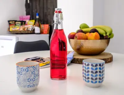 a bottle of red liquid sitting on a table with two cups at FatCow Beach House 43 in Larnaka