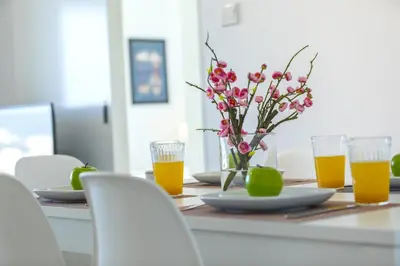a table with a vase of flowers and glasses of orange juice at Mackenzie Zoe Seafront Suite in Larnaka