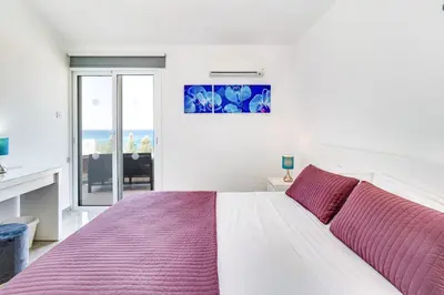a white bedroom with a large bed with purple sheets at Beach Front Aqua Marina by Ezoria Villas in Paralimni