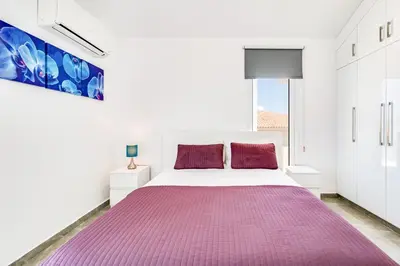 a white bedroom with a large bed with a purple blanket at Beach Front Aqua Marina by Ezoria Villas in Paralimni