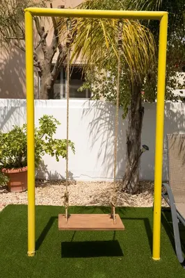 a swing in a garden with yellow poles and grass at Million flowers in Protaras