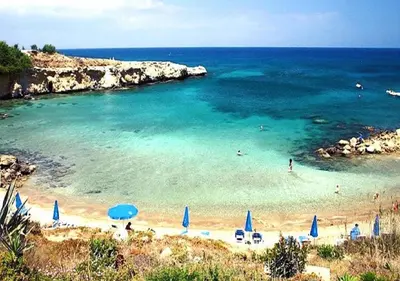 a beach with blue umbrellas and people in the water at Phaedrus Living: Seaside Luxury Villa Anafi in Paralimni
