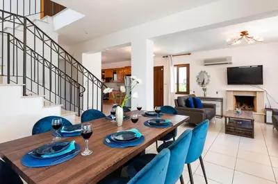 a dining room and living room with a wooden table and blue chairs at Sea Front Costa Blu by Ezoria Villas in Ayia Napa