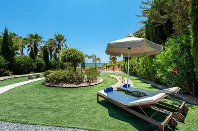 a lounge chair and an umbrella on the grass at Sea Front Costa Blu by Ezoria Villas in Ayia Napa