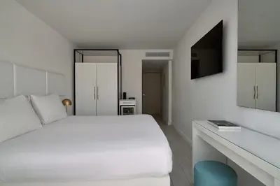 a white bedroom with a white bed and a tv at Hotel Napa Suites (Adults Only) in Ayia Napa