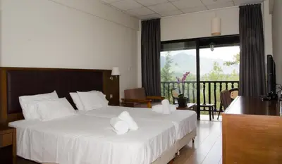 a bedroom with a bed with white sheets and a balcony at Rodon Hotel and Resort in Agros