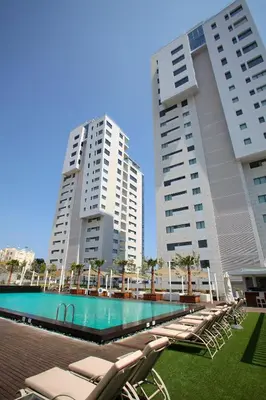 two tall buildings and a swimming pool with lounge chairs at Olympic Residence Deluxe Apartments in Limassol
