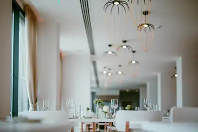 a dining room with white tables and chairs and chandeliers at Lebay Beach Hotel in Larnaka