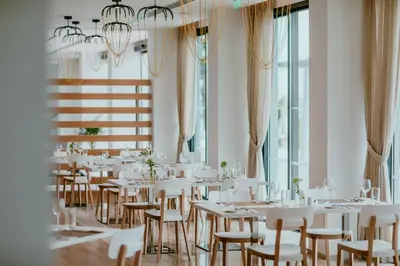 a room with white tables and chairs and windows at Lebay Beach Hotel in Larnaka