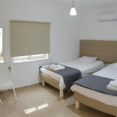 a bedroom with two beds and a chair and a window at CHRIS'S HOLIDAY APT - AYIA NAPA in Ayia Napa