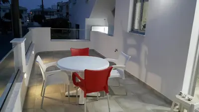 a white table and red chairs on a balcony at CHRIS'S HOLIDAY APT - AYIA NAPA in Ayia Napa
