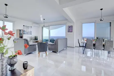 a living room with a table and chairs and windows at Aetopetra Villa in Protaras