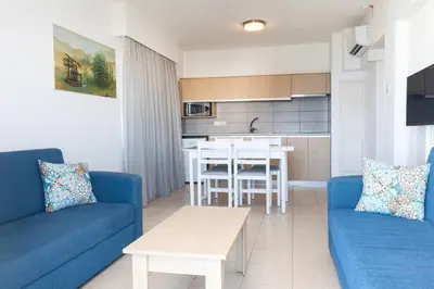 a living room with a blue couch and a kitchen at Vrissaki Hotel Apartments in Protaras