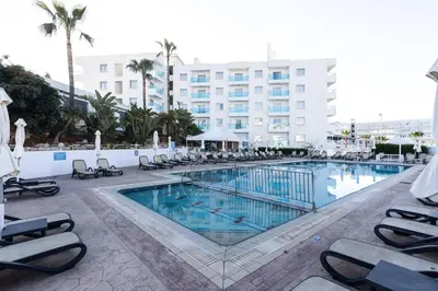a large swimming pool with lounge chairs and a hotel at Vrissaki Hotel Apartments in Protaras
