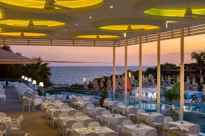 a restaurant with white tables and chairs and the ocean at Melissi Beach Hotel & Spa in Ayia Napa