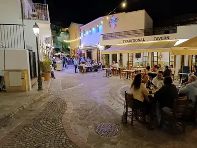 a group of people sitting at tables in a street at night at Rantzo Holiday Apartments in Pissouri