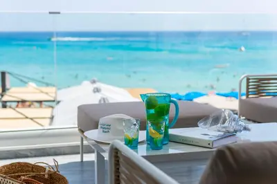 a table with a view of the beach with a drink at Sunprime Protaras Beach - Adults Only in Protaras