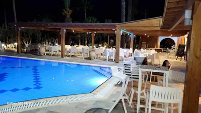 a swimming pool with white chairs and a restaurant at Simos Magic Beach Hotel Apts in Ayia Napa