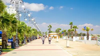 two people walking down a sidewalk with palm trees at Camilla City apartment in Larnaka