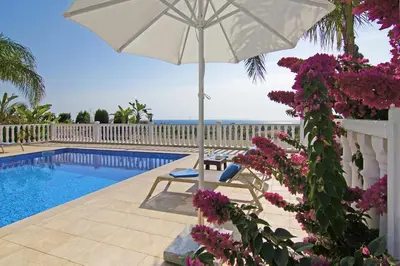 a white umbrella sitting next to a swimming pool with purple flowers at Villa Cleopatra in Ayia Napa