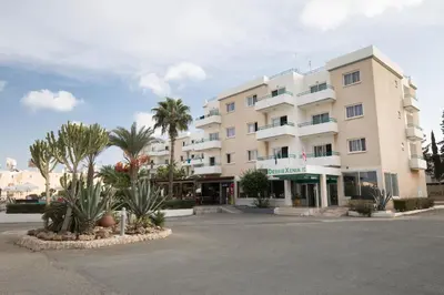a large white building with palm trees in front of it at DebbieXenia Hotel Apartments in Protaras