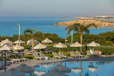 a pool with chairs and umbrellas next to the ocean at NissiBlu Beach Resort in Ayia Napa